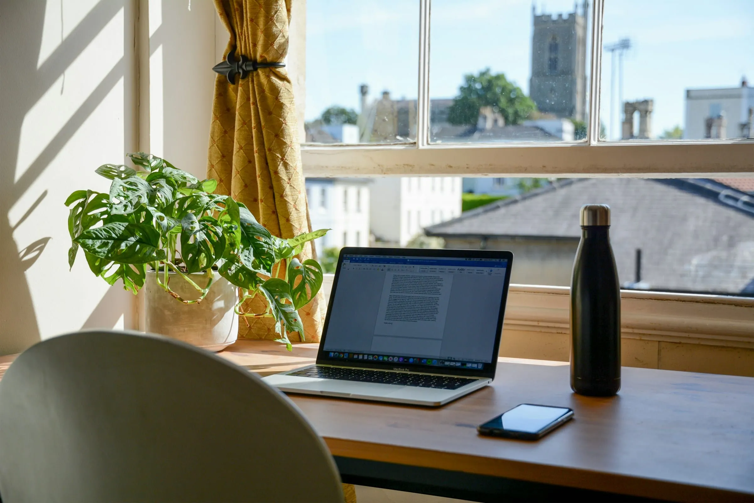 A laptop open on a desk by a window