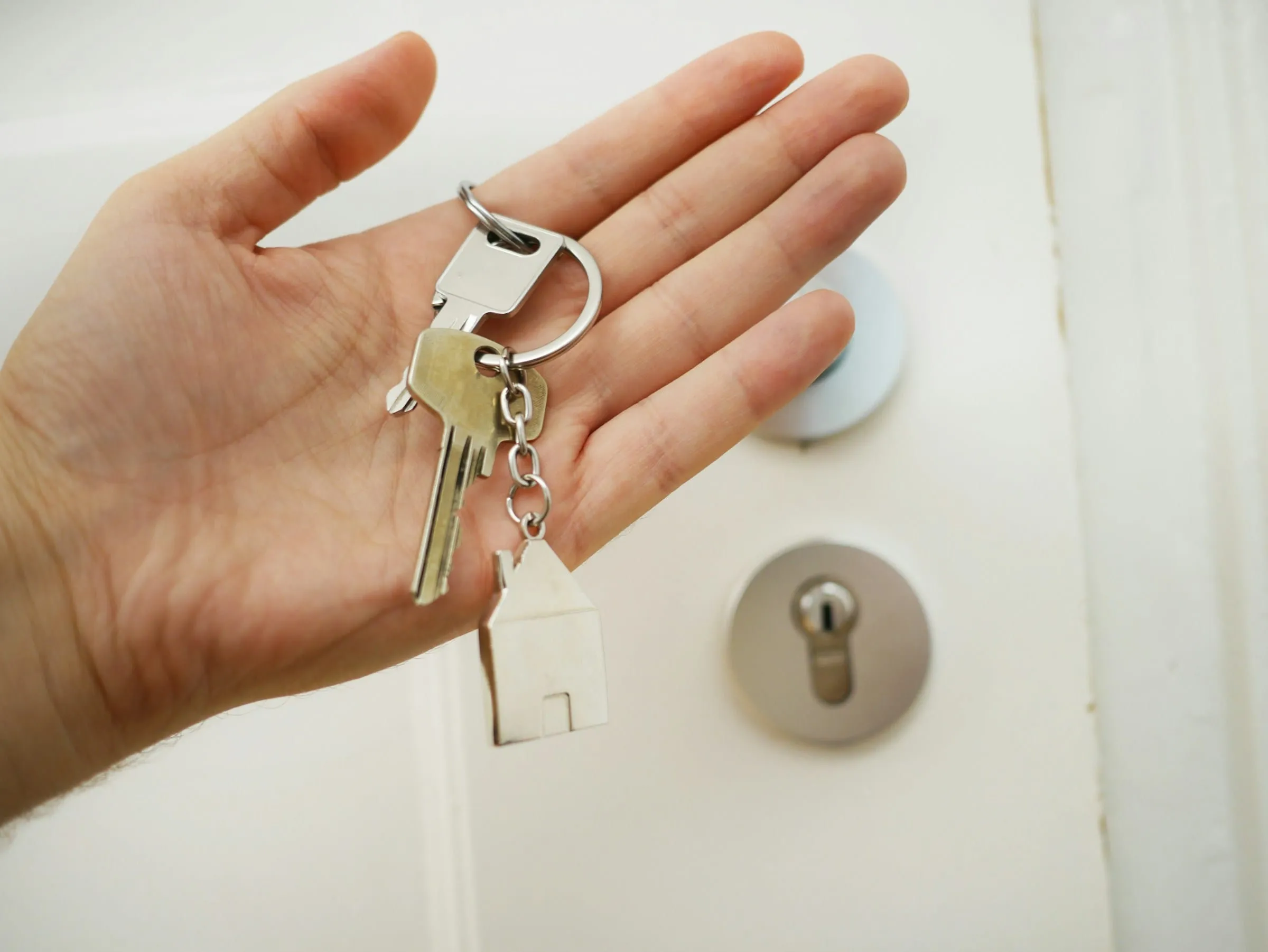 A hand holding a set of house keys beside a front door